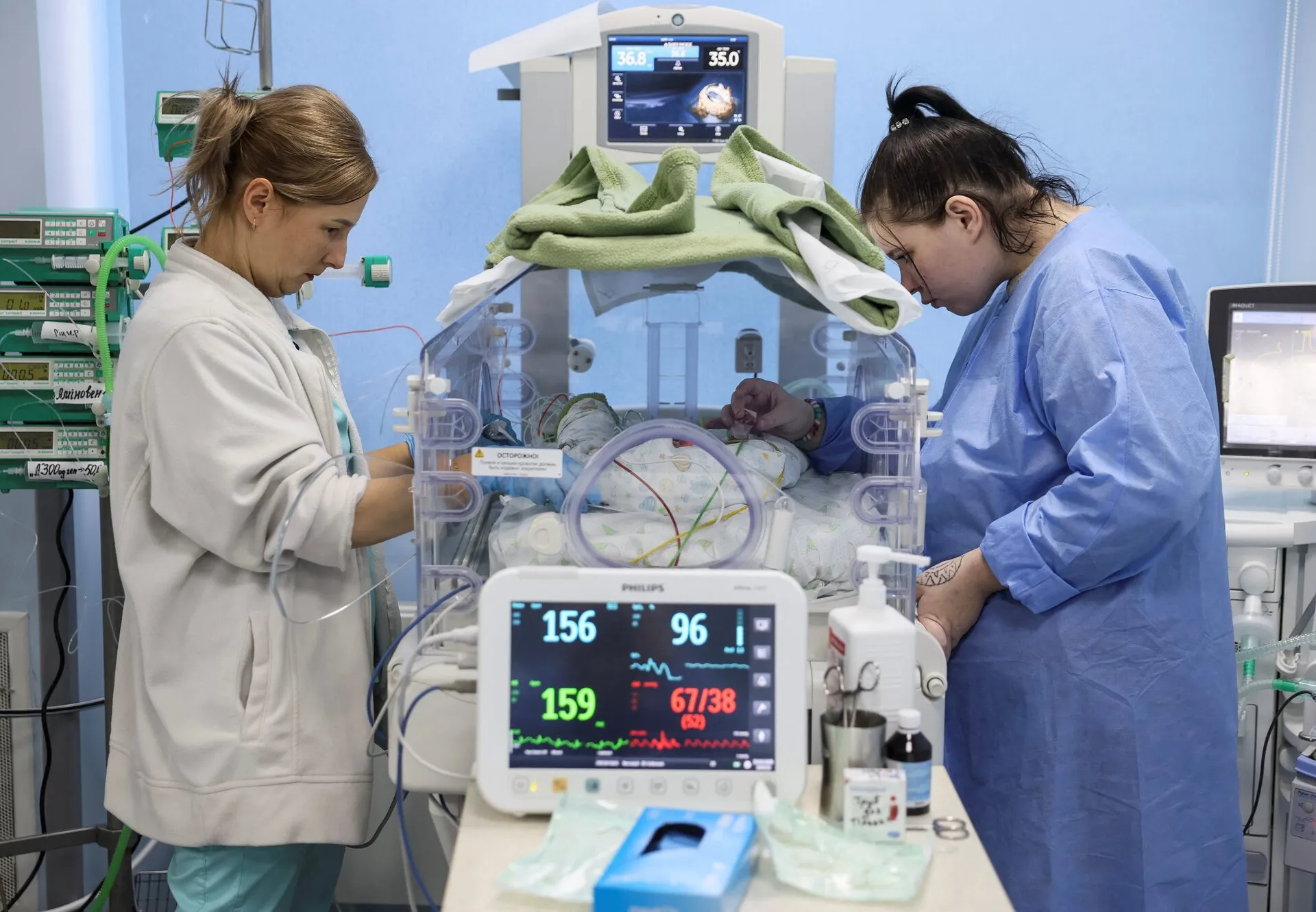 21-річна Анжеліна Шевчук гладить руку своєї новонародженої доньки Вероніки, поки медсестра готує катетер, на тлі нападу Росії на Україну, в Центрі дитячої кардіології та кардіохірургії в Києві, Україна, 15 січня 2025 року